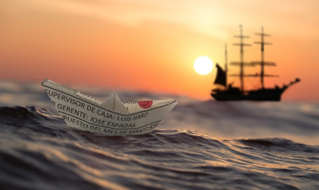 a paper boat next to a big ship in the sunset